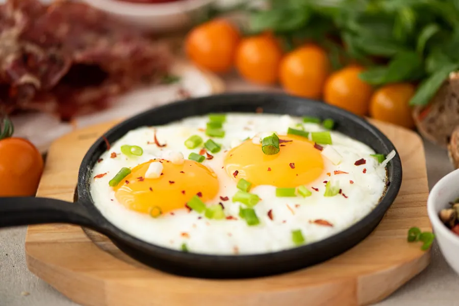 Two perfectly fried whole eggs with runny yolks, garnished with chives, on a white plate.